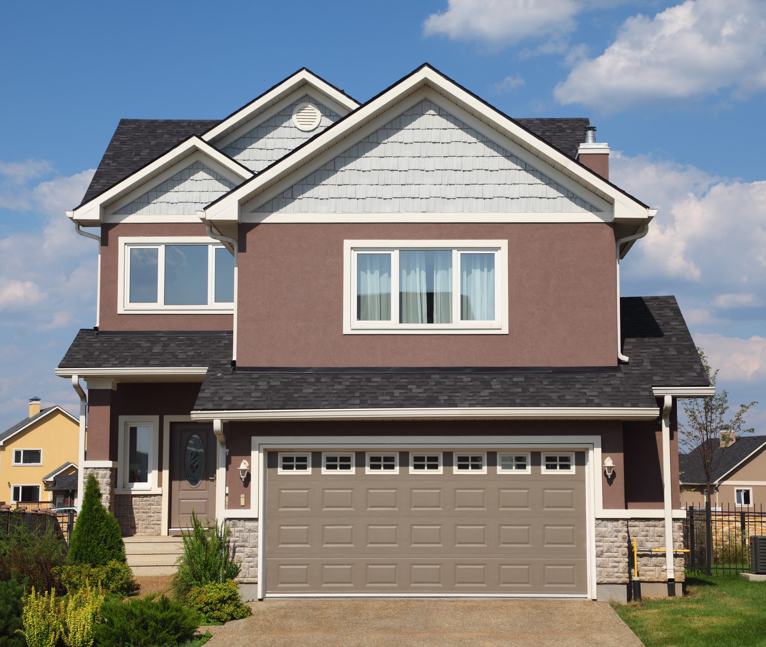 New two-storied white-brown brick cottage with beige garage and white roof.